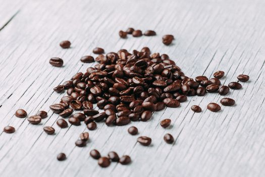 A scattering of coffee beans on a white wooden background.