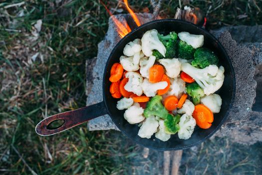 Cauliflower, broccoli and carrot in a pan. Cooking on an open fire. Outdoor food. Grilled vegetables. Food on a camping trip