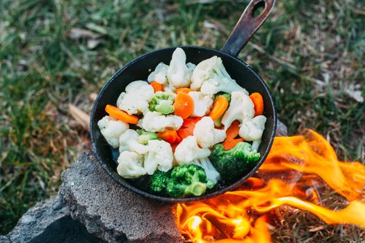 Cauliflower, broccoli and carrot in a pan. Cooking on an open fire. Outdoor food. Grilled vegetables. Food on a camping trip