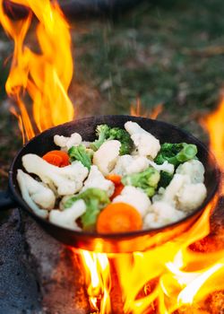 Cauliflower, broccoli and carrot in a pan. Cooking on an open fire. Outdoor food. Grilled vegetables. Food on a camping trip