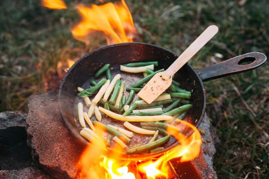 String beans in a pan. Cooking vegetables on an open fire. Food on a camping trip. Wooden spatula in a pan