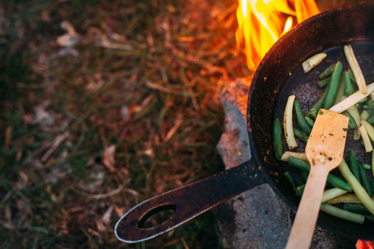 String beans in a pan. Cooking vegetables on an open fire. Food on a camping trip. Wooden spatula in a pan