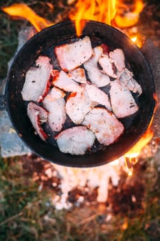 Slices of fried bacon in a pan. Food in a forest camp. Cooking on fire. Picnic in the nature. Grilled food on nature.