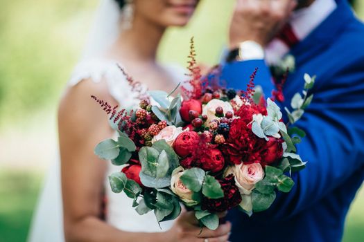 Bouquet in the hand of the bride on the background of a girl and a groom. Bridal bouquet