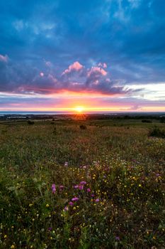 Sunset on the horizon with sky over a rural field and the sea in the background. Sunset, Sunrise over rural meadow field. Countryside landscape with scenic summer dramatic sky in sunset dawn sunrise.