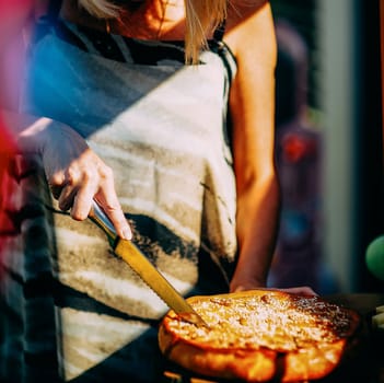 Woman slices a pie under the open skies in the sunlight.