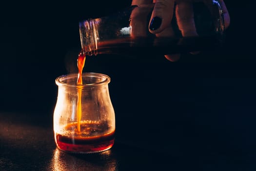 Coffee is poured into a glass jar with milk on a dark background with warm light