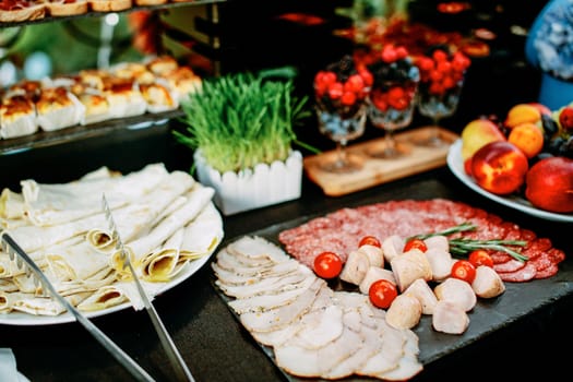 A table with a variety of snacks and slices. Food at an open-air party. Mini burgers and canapes. Decorated table with food flowers and grass.