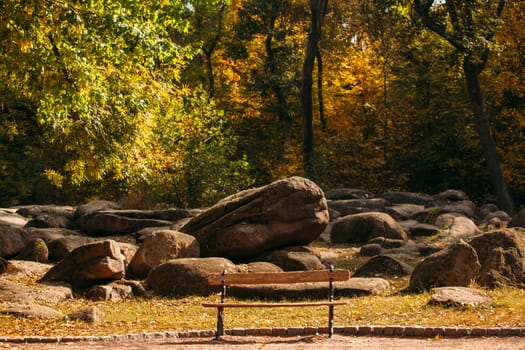 Lonely wooden bench on a background of stones. Beautiful autumn park with large boulders.