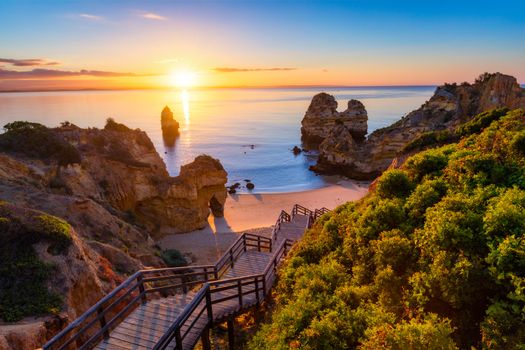 Sunrise at Camilo beach in Lagos, Algarve, Portugal. Wooden footbridge to the beach Praia do Camilo, Portugal. Picturesque view of Praia do Camilo beach in Lagos, Algarve region, Portugal.