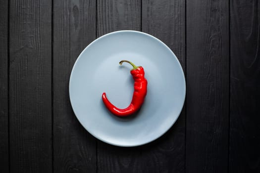 Red hot chili pepper on a gray matte plate that stands on a black wooden background