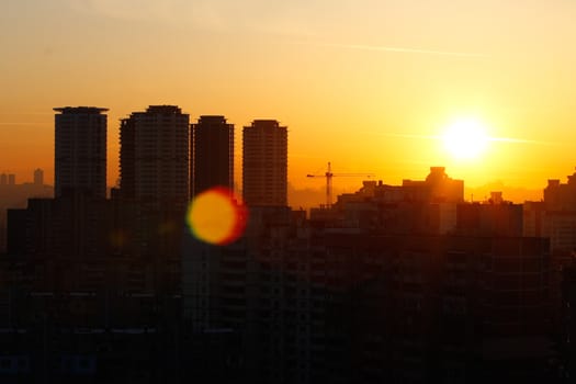 Orange sunset on the background of the city. Silhouette of a construction crane. Photo with a glare from the sun. Panorama of the city.