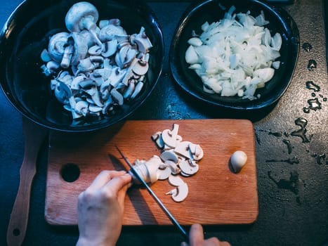 Cutting mushrooms before cooking. Hands with a knife. Plate with chopped mushrooms and onions.