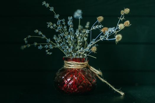 Dry bouquet with field plants in an old red vase on a wooden dark background