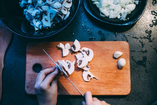 Cutting mushrooms before cooking. Hands with a knife. Plate with chopped mushrooms and onions.