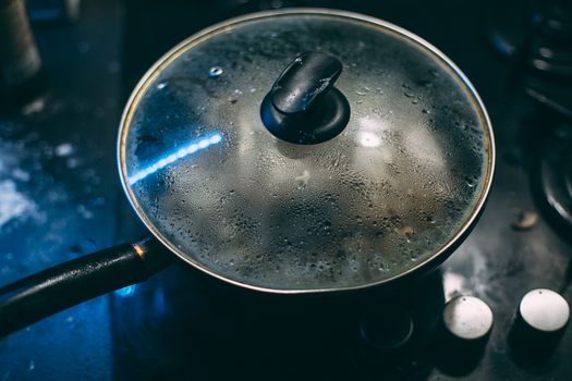 Black pan with a transparent lid on fire. Black plate