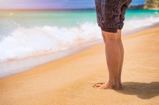 Closeup on leg of young woman standing on sea shore. Woman legs and feet walking on the sand of the beach with the sea water in the background. Woman standing on the beach with wave sea.