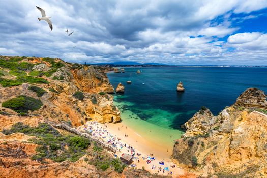 Camilo beach (Praia do Camilo) with seagulls flying over the rocks in Lagos, Algarve, Portugal. Wooden footbridge to the beach Praia do Camilo, Algarve, Portugal.
