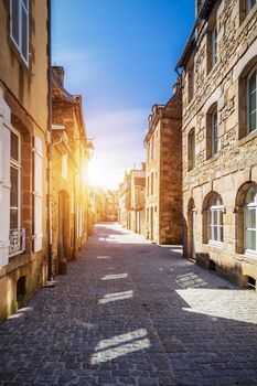 Beautiful view of scenic narrow alley with historic traditional houses and cobbled street in an old town of Dinan with blue sky and clouds. Brittany (Bretagne), France