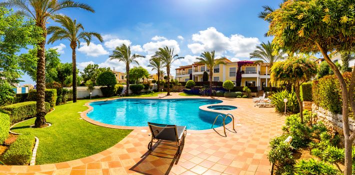 Swimming pool, sun-loungers and palm trees during a warm sunny day, paradise destination for vacations. Backyard swimming pool with garden full of palm trees and flowers. Backyard with swimming pool.