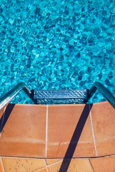 Swimming pool with stair. Grab bars ladder in the blue swimming pool. Poolside with blue clear water and ladder. Stair at the side of swimming pool, summer concept.