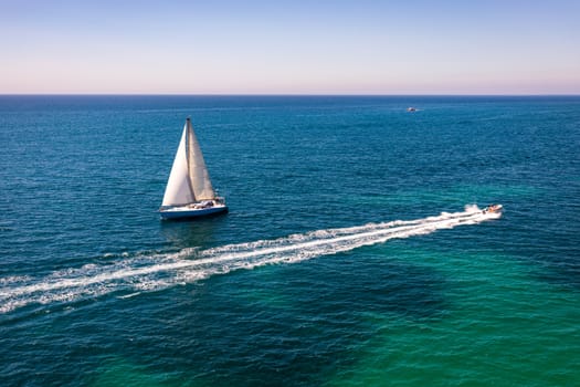 White sail boat isolated in blue sea water. Sailboat in the sea in the sunlight, luxury summer adventure, active vacation in Mediterranean sea. Yacht sailing on opened sea. Sailing boat. 