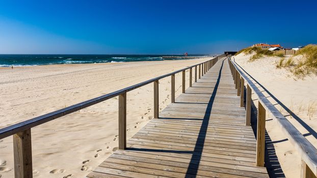 Wooden path at Costa Nova d'Aveiro, Portugal, over sand dunes with ocean view, summer evening. Wooden footbridge of Costa Nova beach in a sunny day. Aveiro, Portugal. 