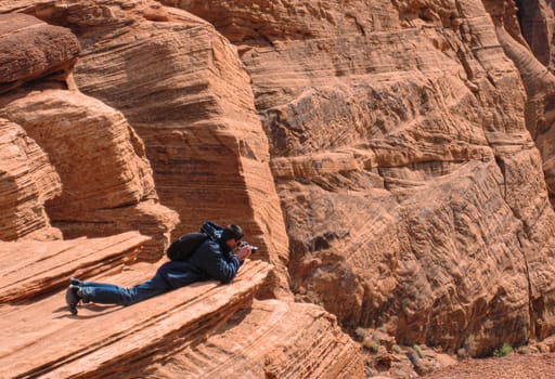 Photographer lying down over the edge of horseshoe bend and taking a photo in a danger situation.