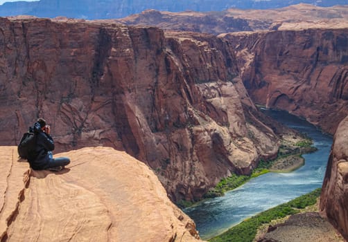 Photographer sitting over the edge of horseshoe bend and taking a photo in a danger situation.