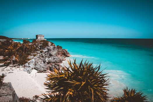 Mayan Temple of the Wind God, perched on a rocky cliff, Tulum, Mexico. Teal and oragne