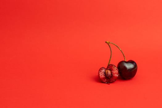 Two cherries on the right on a deep red background. Bitten cherry with stone.