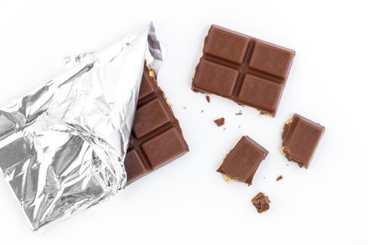Bar of milk chocolate with hazelnuts, with pieces and flakes scattered after tasting.