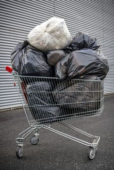 A shopping cart full of garbage bags. A representation of consumerism and trash food.