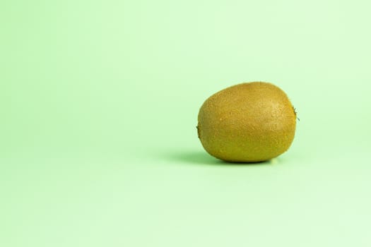 Whole unpeeled ripe kiwi fruit on a turquoise green background on the right