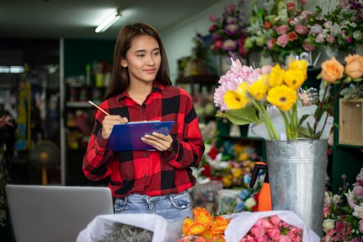 Asian Woman Florist Small Business Flower Shop Owner working and Holding A Clipboard  Writing to take orders for her store.