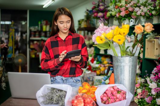 Asian Woman Florist Small Business Flower Shop Owner holding calculator for working to take orders for her store.
