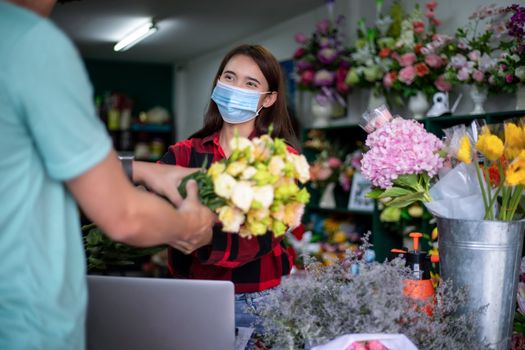 Asian Woman wearing  face mask or protective mask against coronavirus crisis, Florist owner of a small florist business holding flowers for delivery to customers at her store