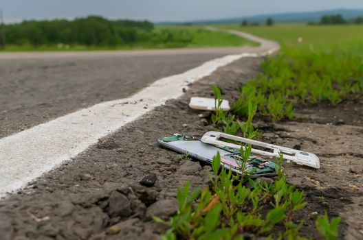 View of a mobile phone lying on the asphalt on a country road in cloudy weather