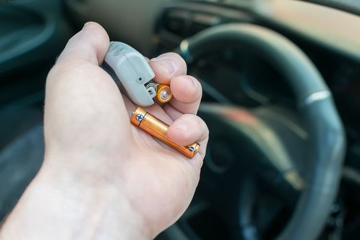 the hand of the person who is in the car holds the disassembled alarm keychain and a new battery for replacement