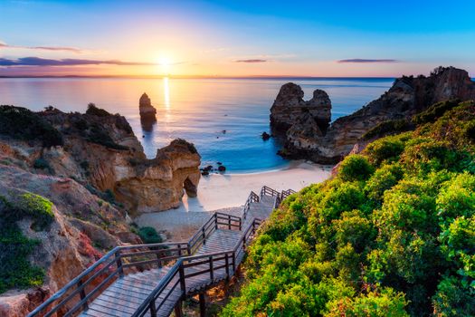 Sunrise at Camilo beach in Lagos, Algarve, Portugal. Wooden footbridge to the beach Praia do Camilo, Portugal. Picturesque view of Praia do Camilo beach in Lagos, Algarve region, Portugal.