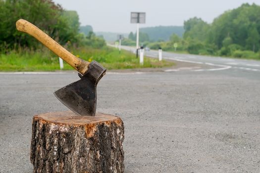 view of the ax, which is stick in a wooden chock on the background of a country road