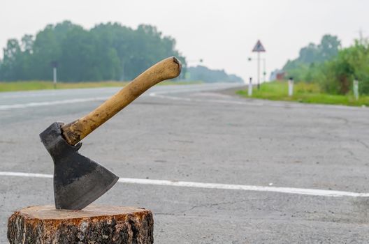 view of the ax, which is stick in a wooden chock on the background of a country road