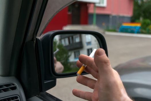 close-up of a cigarette in the hand of a man in the car, who watches the entrance door of the house