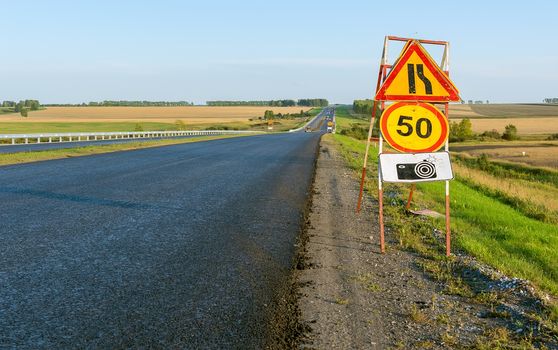 road sign road repair, speed limits and warnings about the camera fixing violations on the background of a country highway in the autumn