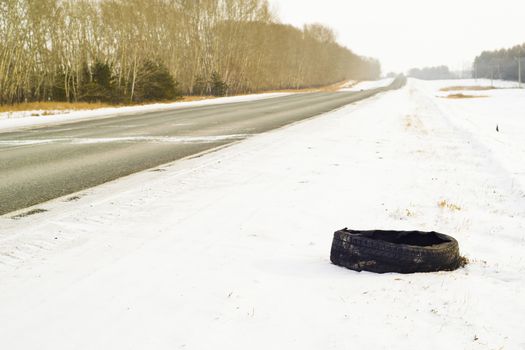 a torn car tire from a truck lies in the snow on the side of the road