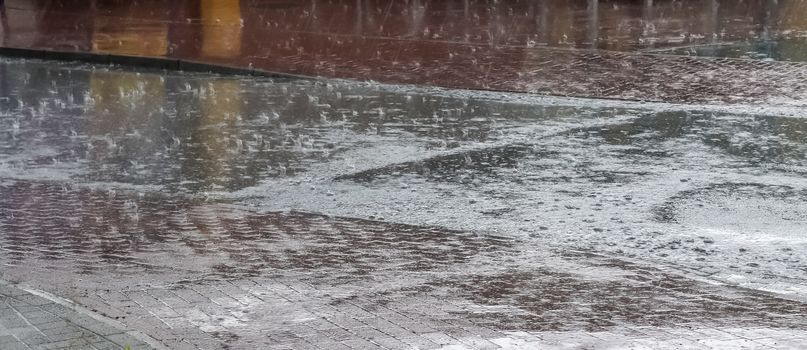 Heavy rain drops falling on city street during downpour. Wet ashpalt road texture.
