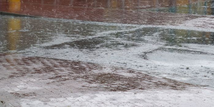 Heavy rain drops falling on city street during downpour. Wet ashpalt road texture.