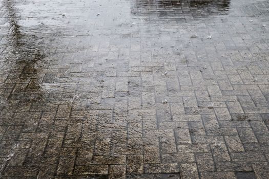 Heavy rain drops falling on city street during downpour. Wet ashpalt road texture.