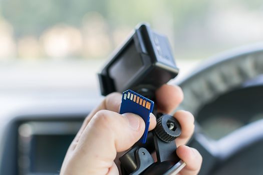 the hand of a male car driver that holds a car DVR recording incidents and a memory card to it