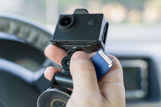 the hand of a male car driver that holds a car DVR recording incidents and a memory card to it